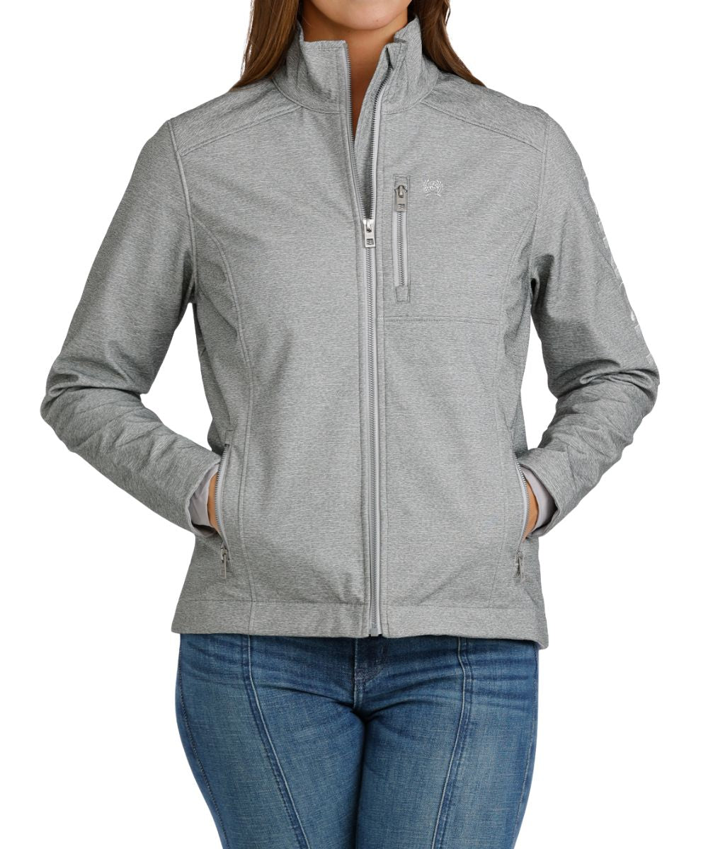 Front view of the women's grey Cinch bonded softshell concealed carry jacket featuring the zip-up closure, zippered hand and chest pockets, mock collar, and the metallic logo embroidery