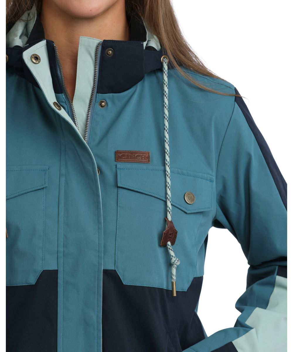 Close-up view of the women's teal color blocked cropped chore jacket featuring the offset snap flap chest pockets, removable hood with a contrast drawcord, and storm flap