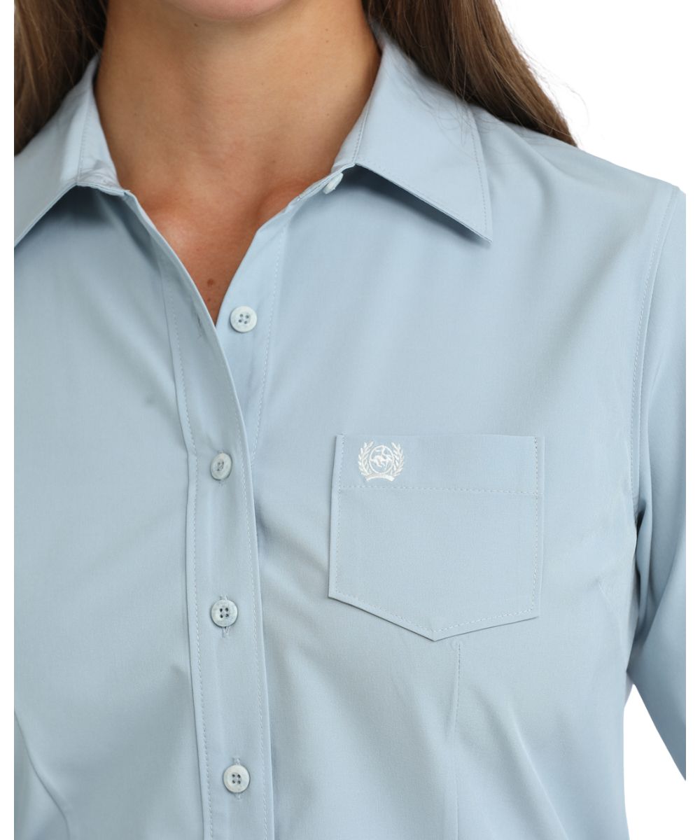 Close-up view of the women's solid print light blue button down shirt featuring the marble buttons and chest pocket
