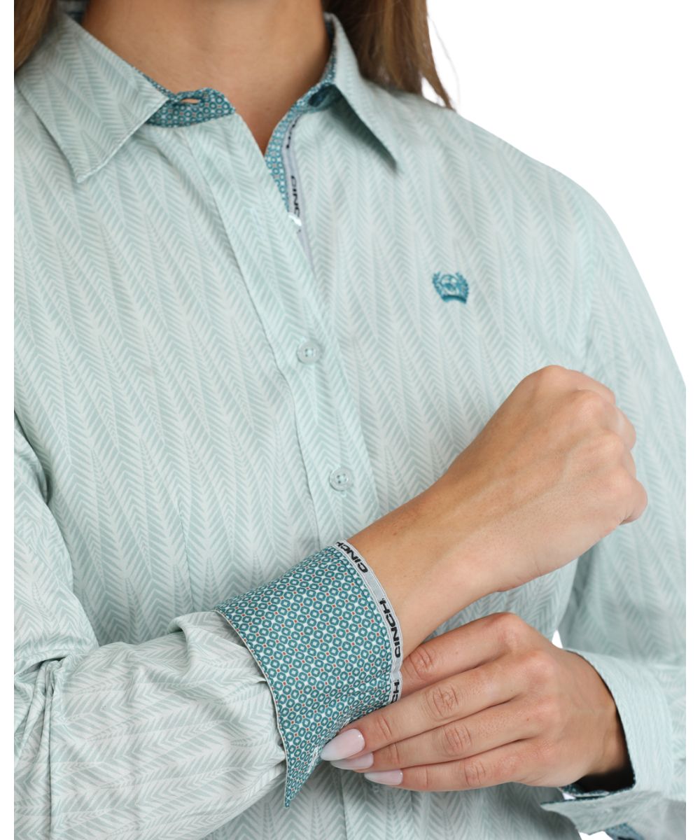 Close-up view of the light blue button down featuring the geometric print, logo embroidery on chest, and contrast interior trim