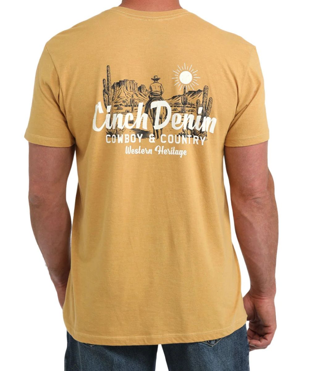 A man wearing a mustard yellow t-shirt from the back, featuring a black and white graphic with the text 'Cinch Denim' and 'Cowboy & Country Western Heritage'.