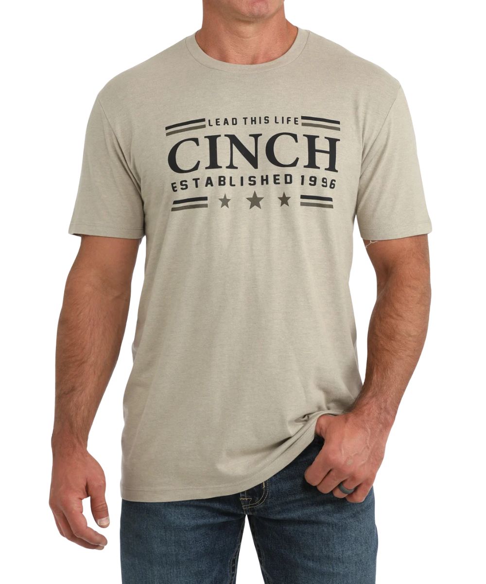 Front view of the men's khaki Cinch tee featuring the short sleeves, crew neck, and a front screen print that reads: "Cinch Lead This Life Established 1996"