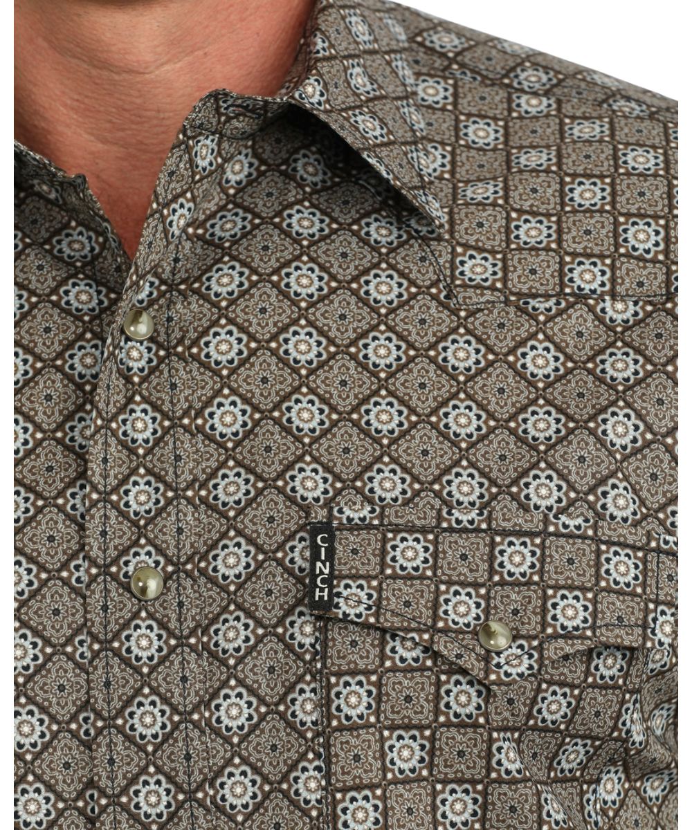 Close-up view of the geometric print, contrast topstitch, brown marble snaps, and single point snap flap chest pockets with logo label
