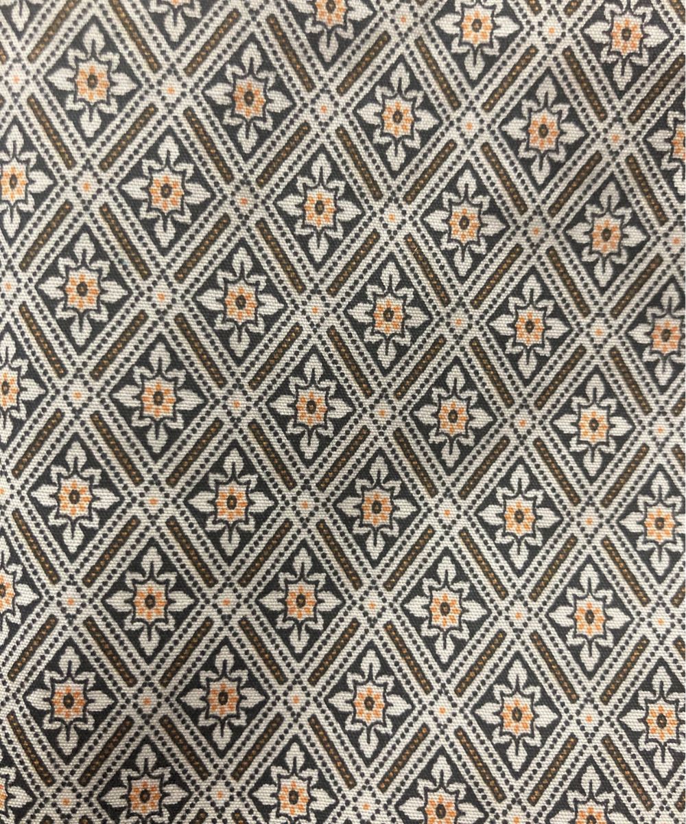 A close-up of a woven fabric with a repeating geometric diamond pattern in brown, beige, and muted orange.