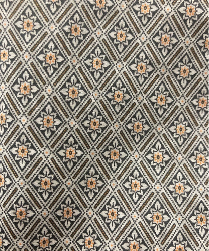 A close-up of a woven fabric with a repeating geometric diamond pattern in brown, beige, and muted orange.