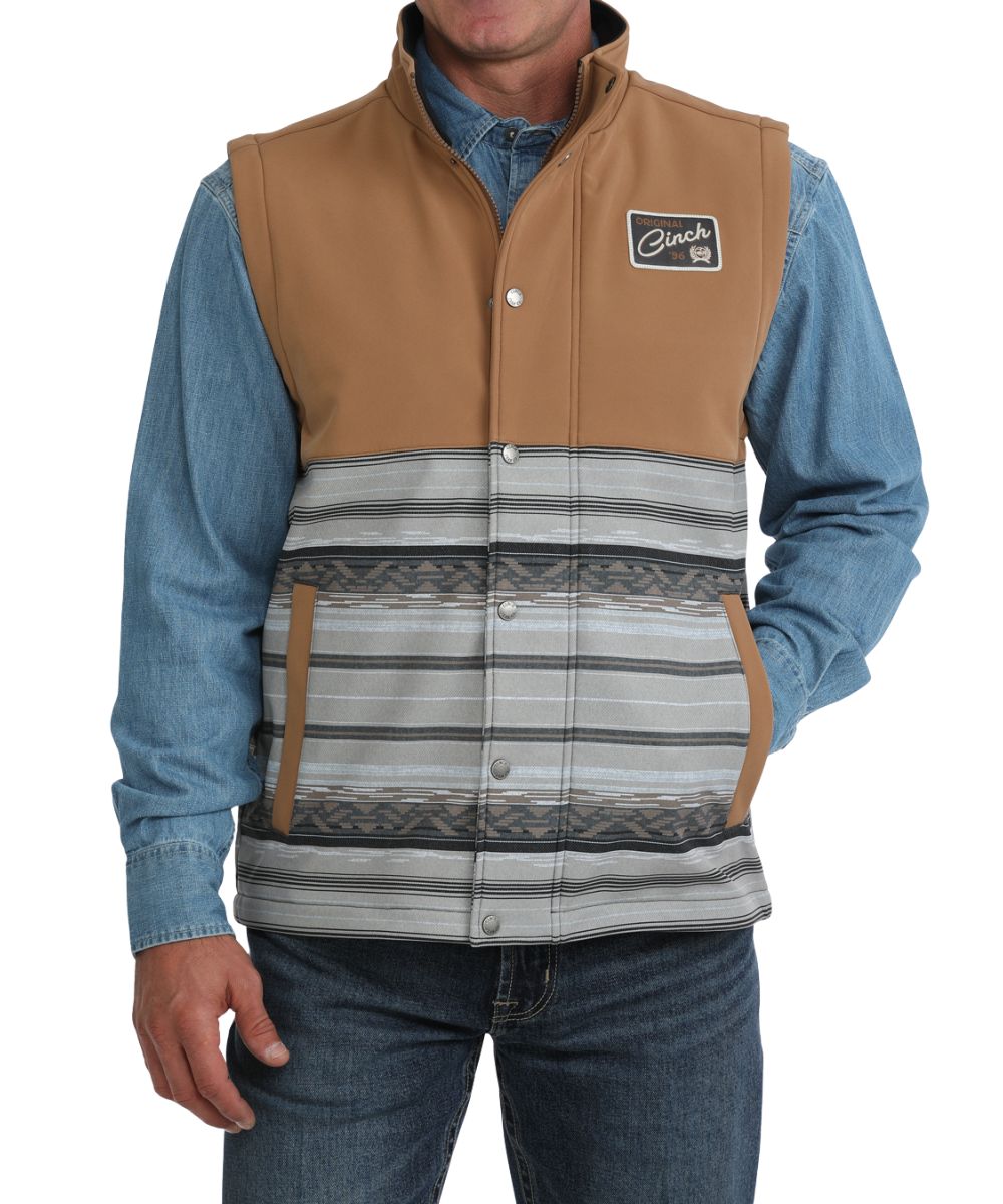 Front view of the men's tan Cinch bonded vest featuring the color blocked design with a tan upper and grey serape striped lower body, hand pockets, zip closure with a snap storm flap, and mock collar