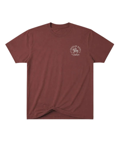 A short-sleeve crewneck t-shirt in a muted reddish-brown or maroon color, featuring a small white circular graphic on the left chest with the text 'SHOULDA BEEN A COWBOY'. The bottom hem is tied in a knot, and the shirt is photographed flat against a solid white background.