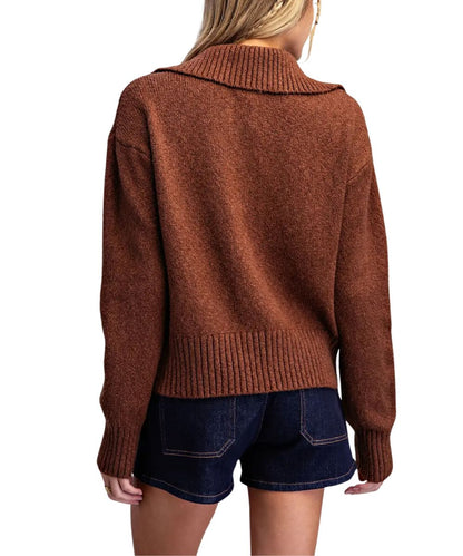 A woman shown from the back wearing a brown knit sweater with a wide ribbed collar and dark denim shorts against a plain white background.