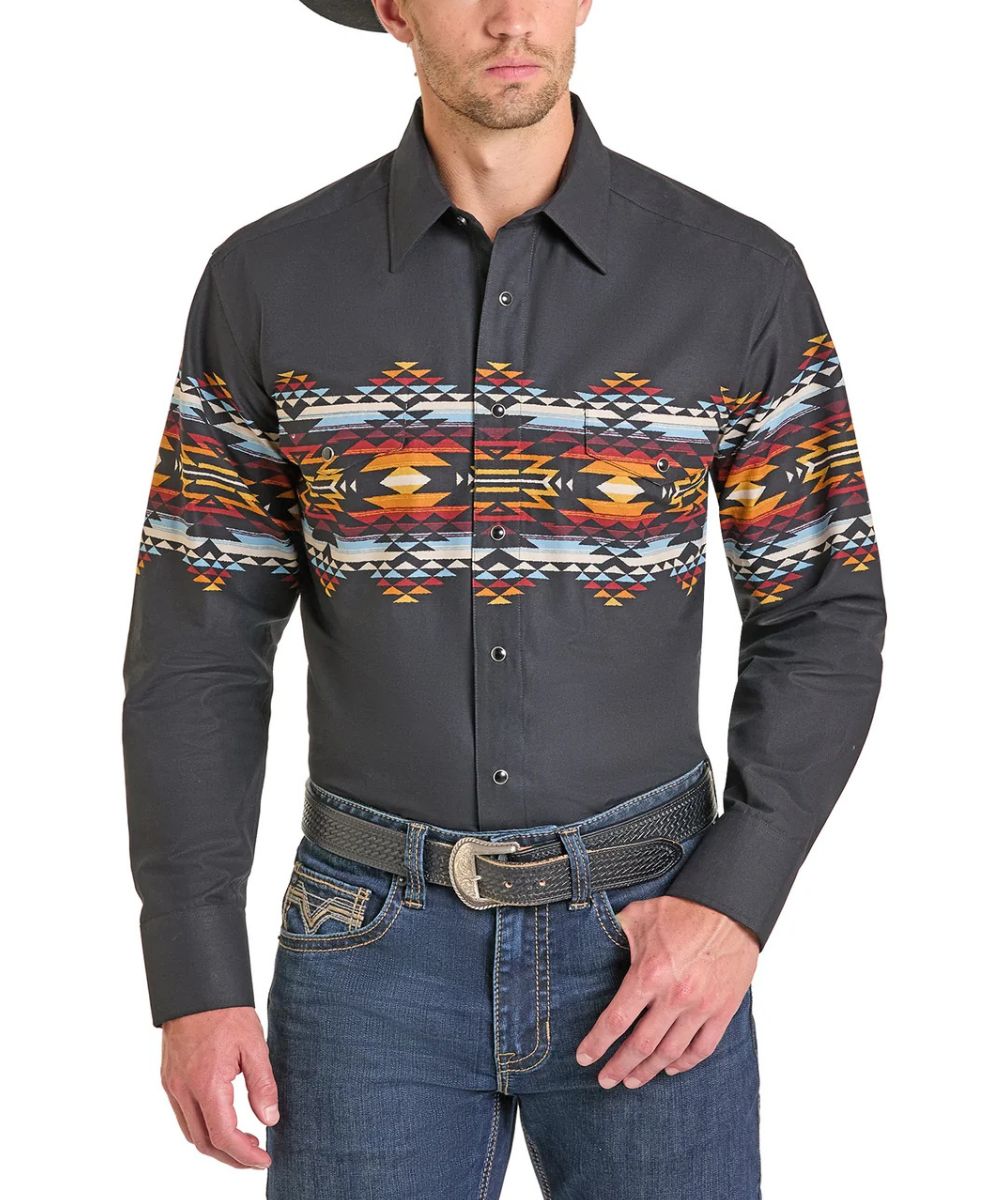 A man wearing a dark gray long-sleeve western shirt with a colorful geometric Southwestern pattern across the chest and upper sleeves, paired with blue jeans and a textured belt.