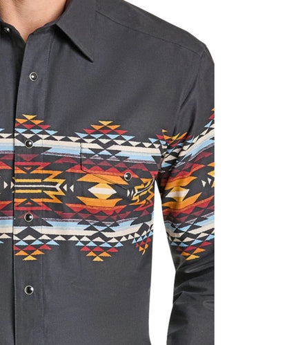 A close-up of a men's long-sleeve button-up shirt with a dark charcoal gray base and a vibrant geometric Southwestern pattern across the chest and sleeves, featuring red, orange, yellow, black, and light blue stripes.