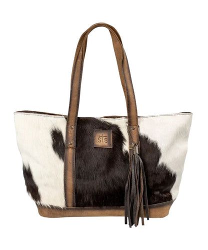 Front view of the women's brown STS Cowhide Cheyenne Tote featuring the hair-on-hide front with a STS branded leather patch, removable decorative tassel, and dual leather carrying handles