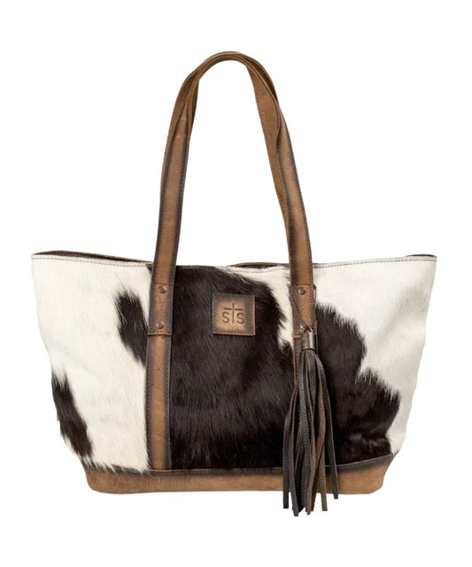 Front view of the women's brown STS Cowhide Cheyenne Tote featuring the hair-on-hide front with a STS branded leather patch, removable decorative tassel, and dual leather carrying handles