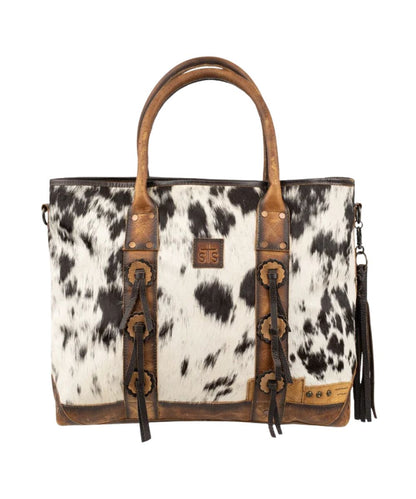 Front view of the women's brown STS Guadalupe Cowhide All-In Tote featuring the hair-on-hide front with a STS branded leather patch, leather concho accents, dual leather carry handles, and a removable leather tassel