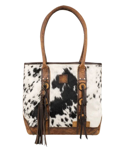 Front view of the women's brown STS Guadalupe Cowhide Palamino Tote Bag featuring the hair-on-hide front with a STS branded leather patch, dual rolled leather carry handles, front leather conchos with fringe accents, and a removable leather tassel