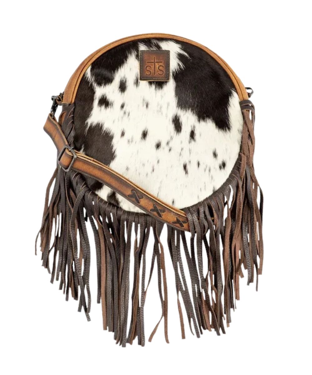 Front view of the women's brown STS Guadalupe Cowhide Sage Circle Crossbody featuring the hair-on-hide front, fringed bottom, STS branded patch, and a removable/adjustable leather crossbody strap