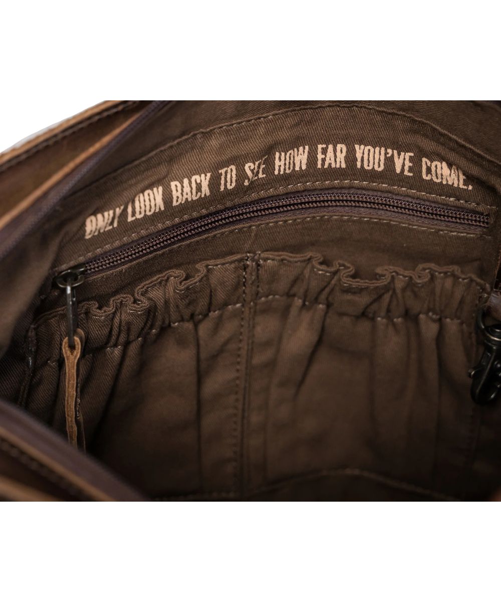 Interior view of the women's shoulder bag featuring the zip closure, interior scrunch and zip pockets, concealed carry pocket, and a quote that reads: "Only Look Back To See How Far You've Come."