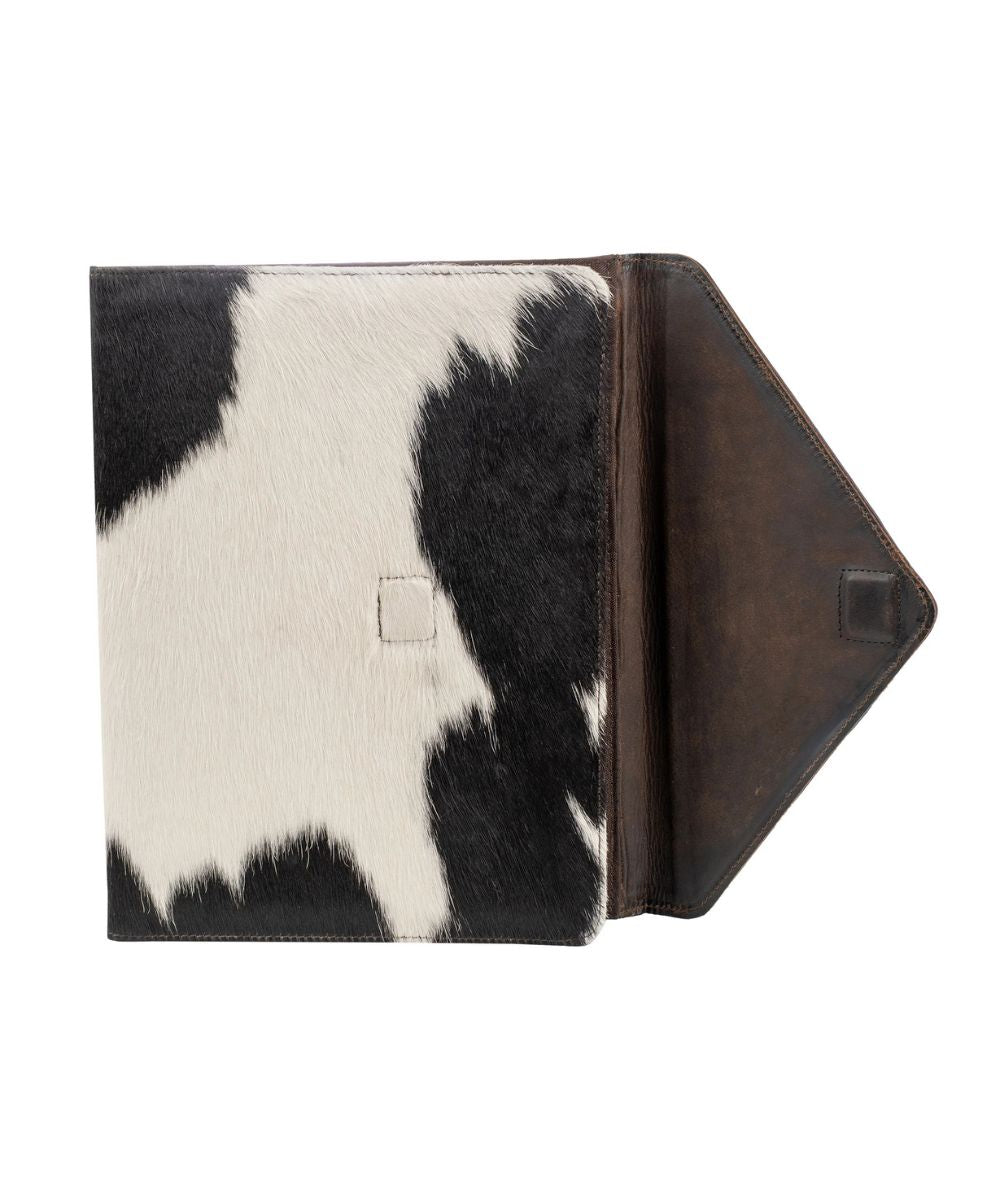 A tablet sleeve featuring a black and white cowhide pattern on the front cover and a dark brown leather interior flap, shown open against a plain white background.