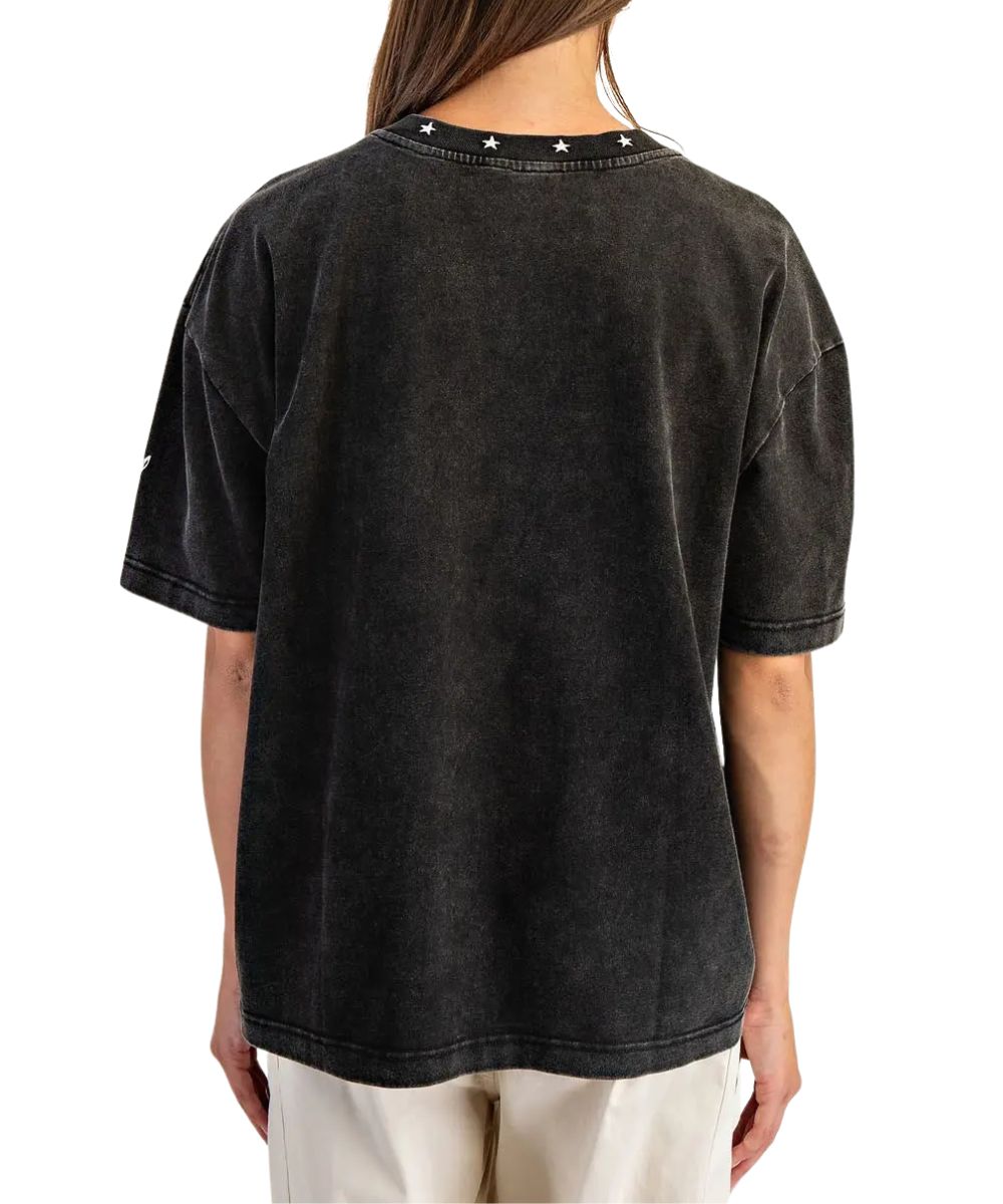 A person shown from the back wearing a faded black short-sleeve t-shirt with small white star details along the inner neckline, paired with off-white pants, against a plain white background.