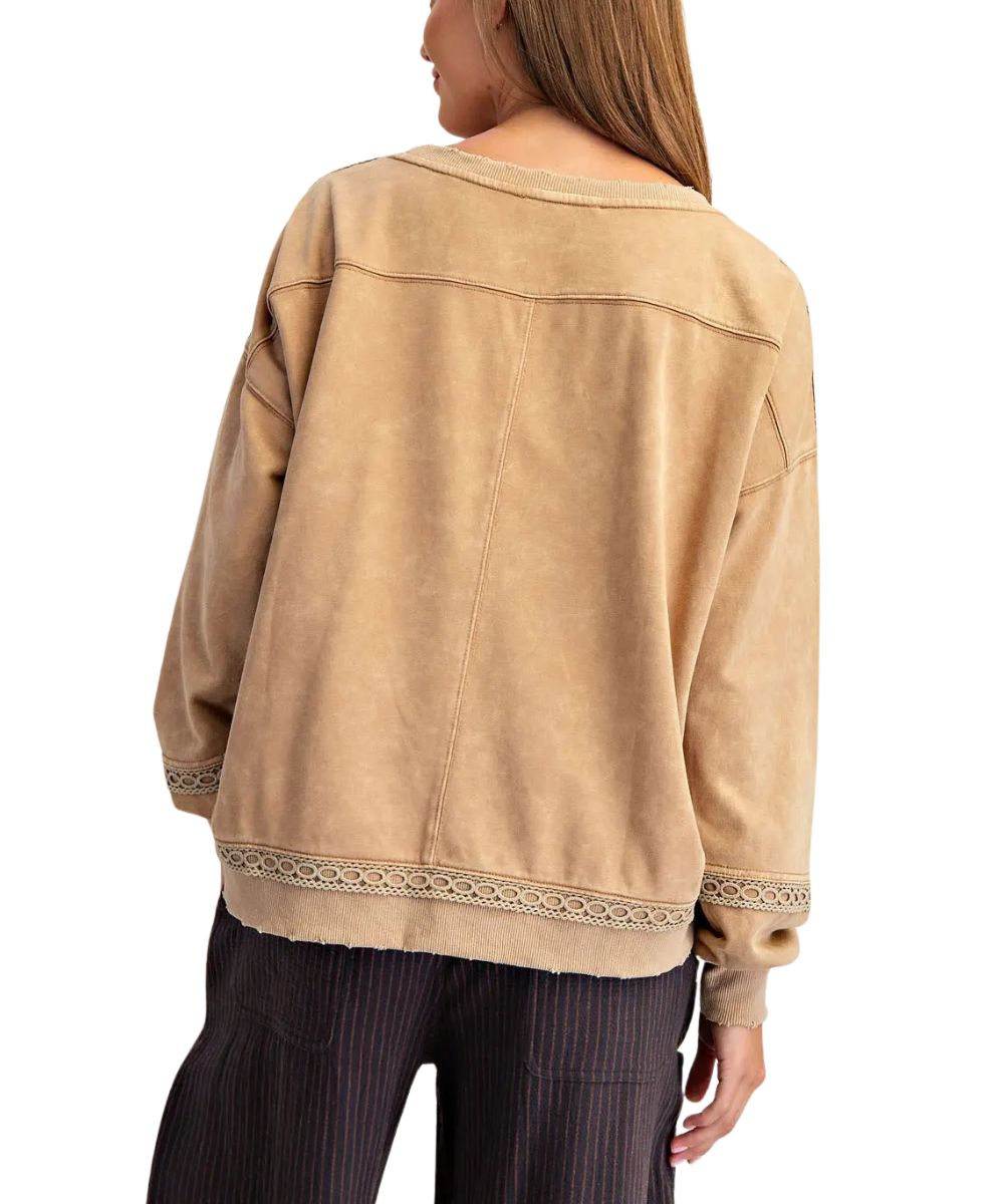 A woman shown from the back wearing a brown long-sleeve top with decorative lace trim at the cuffs and hem, paired with dark pinstriped pants, against a plain white background.