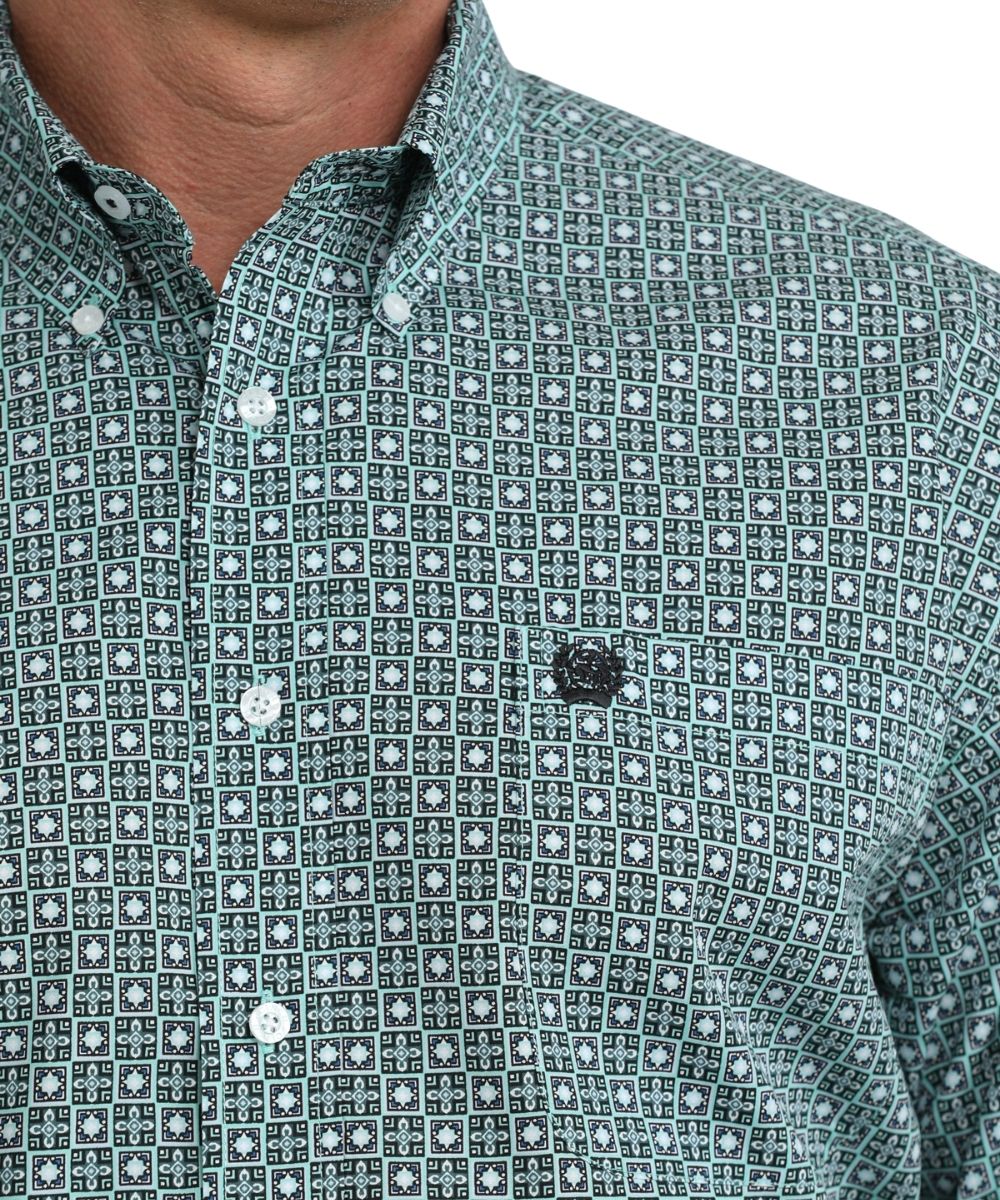 Close up view of single open pocket with Cinch embroidered logo and of button down collar of green and white geometric print shirt